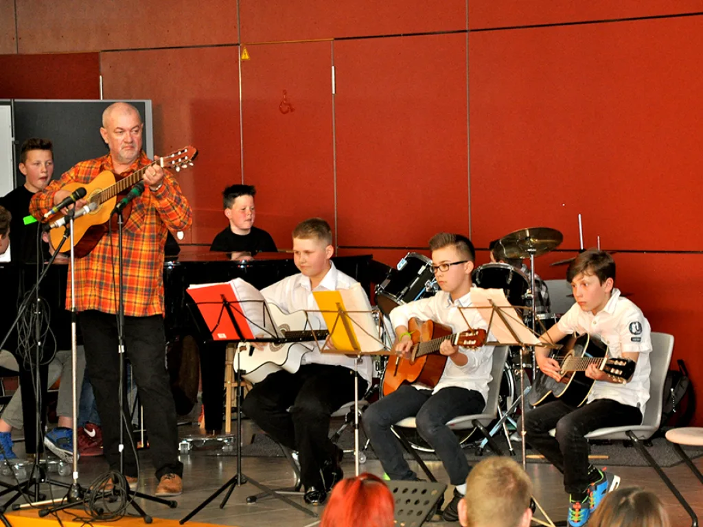 Eine Band aus Jugendlichen und einem Erwachsenen spielt Gitarre und Schlagzeug.